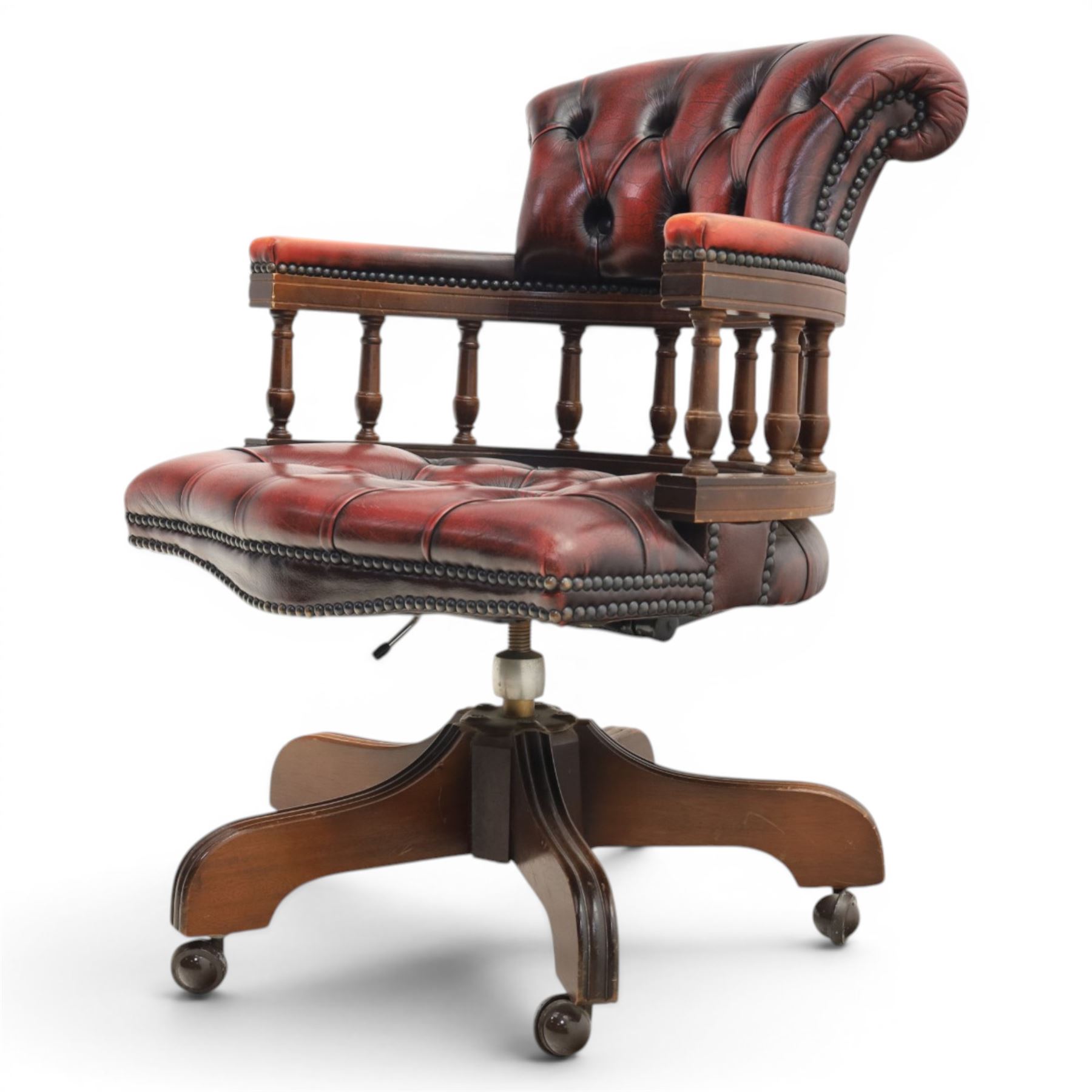 Captains swivel desk chair upholstered in oxblood leather, buttoned back and seat, shaped arm bow raised on turned spindles, five spoke base raised on castors