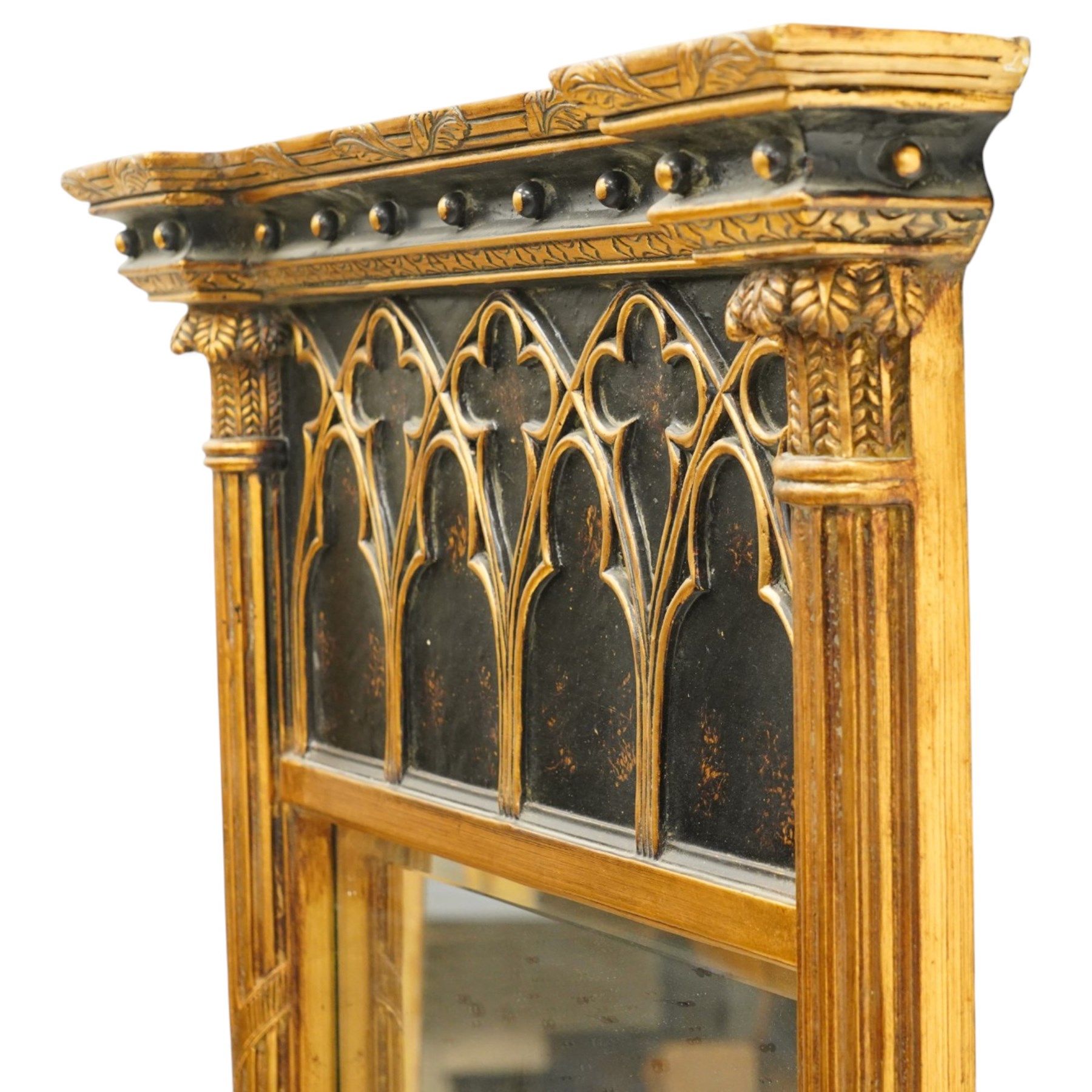 Tall Gothic Revival ebonised and gilt pier mirror, the projecting cornice with foliate ornament and applied spherical mounts, over a Gothic tracery frieze with trefoil motifs, the bevelled rectangular plate flanked by fluted Neoclassical columns with acanthus capitals, on a stepped ebonised and gilt plinth base with globular mounts