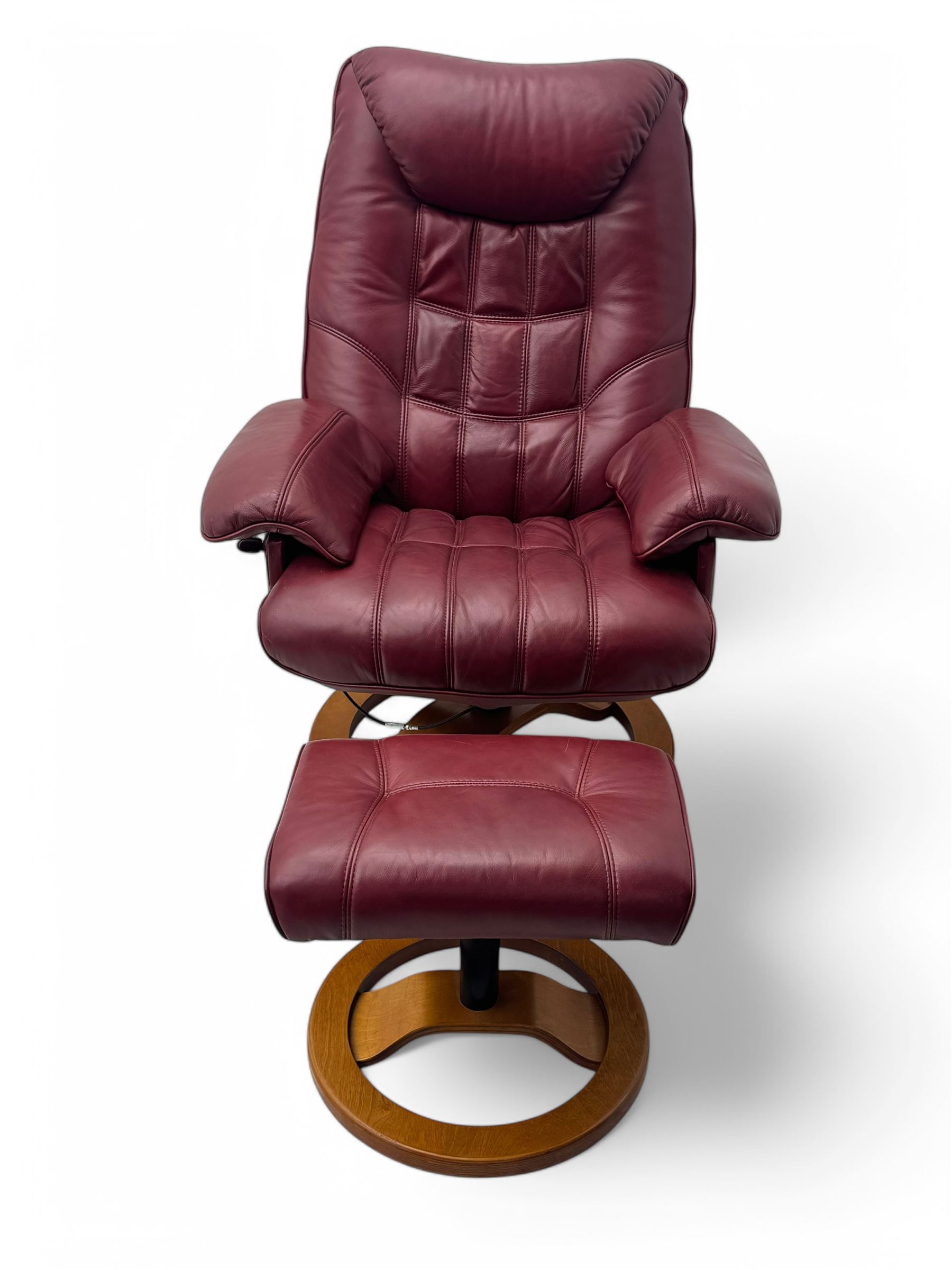 Contemporary burgundy leather reclining armchair and footstool, featuring segmented upholstered cushions and padded armrests, each piece mounted on a circular laminated wood base