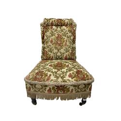 Late 19th century nursing chair, upholstered in foliate patterned fabric with fringing an sprung seat, raised on turned supports with brass and ceramic castors