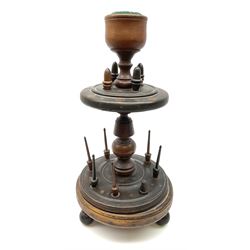 A 19th century turned oak and fruitwood bobbin stand, upon three turned feet supporting a stepped lower platform with spindles, leading to turned stem, further graduated platform with acorn finials and goblet shaped pin cushion, overall H36.5cm.