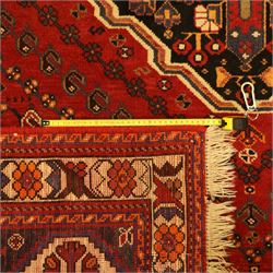 Persian Shiraz rug, hand-knotted tribal rug, bold geometric central medallion, set within a large hexagonal crimson field with angular stepped corners in dark blue, with boteh motifs, rosettes, and other tribal symbols arranged in diagonal rows, the corners with indigo spandrels decorated with zoomorphic and arboreal motifs, main border composed of a floral meander motif with large rosette, flanked guard borders with vine and leaf motifs 