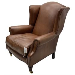 Georgian design wingback armchair, upholstered in brown leather with stud band and piping, turned and fluted front feet on brass cups and castors