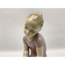 Large Nao figure modelled as a young girl seated upon a rock holding a rose, H30cm