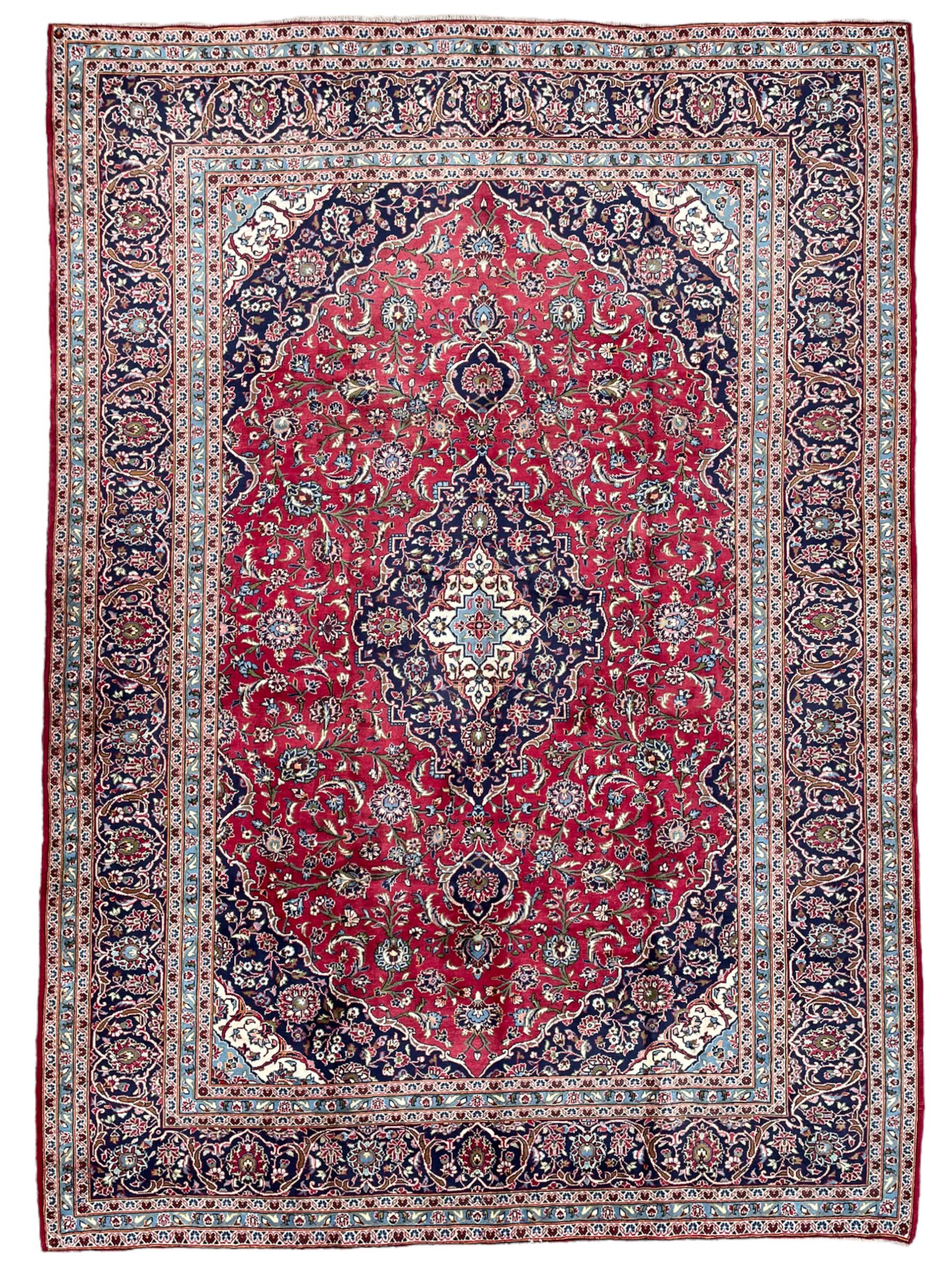 Central Persian Kashan crimson ground carpet, central  floral pole medallion with matching spandrels within a field of scrolling palmette motifs and foliage, the heavily banded indigo border with repeating plant motifs interlaced with scrolled branches