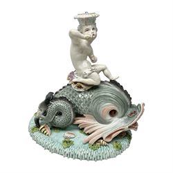 Early 20th century continental centrepiece, modelled as a putti riding a dolphin, upon a blue base decorated in relief with seaweed, flowers and shells, with spurious mark beneath