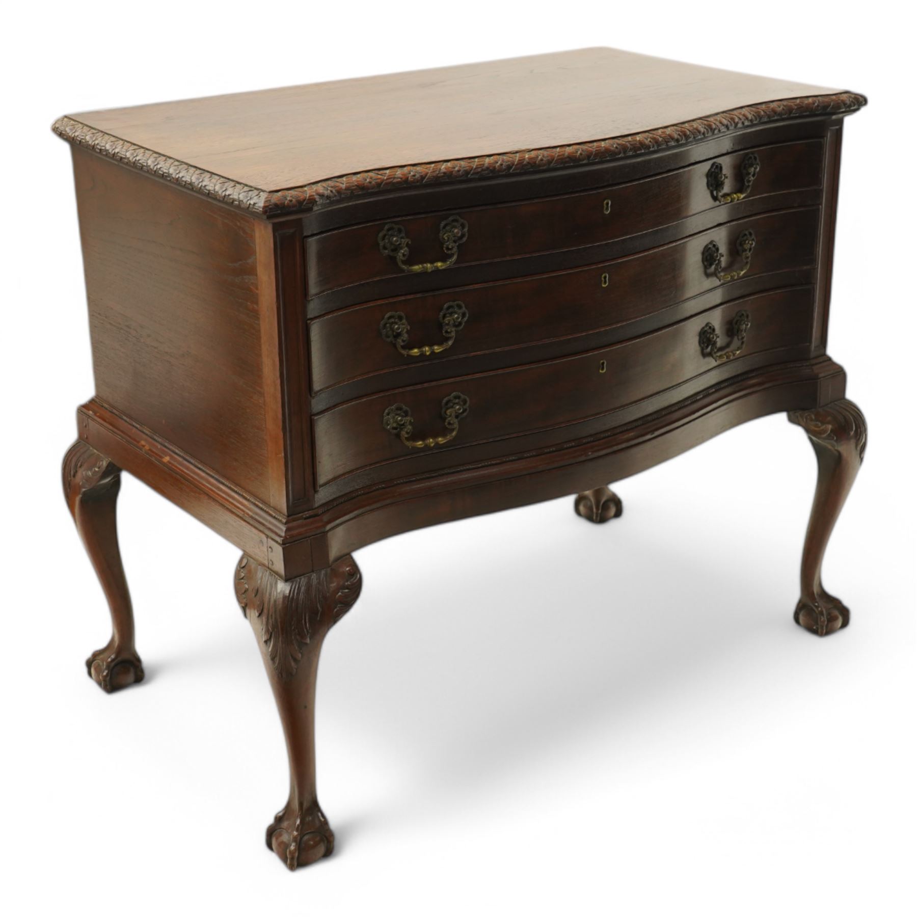 20th century oak and mahogany serpentine chest, the moulded top carved with trailing crossed ribbon and flower heads, fitted with three long cock-beaded drawers, ornate cast gilt metal handles, on acanthus leaf carved cabriole supports with ball and claw feet 