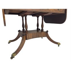 Regency period mahogany drop-leaf sofa table, rectangular top fitted with two cockbeaded drawers with ebony stringing, raised on turned columns united by quadrupod base, the sabre supports terminating in brass cups and castors