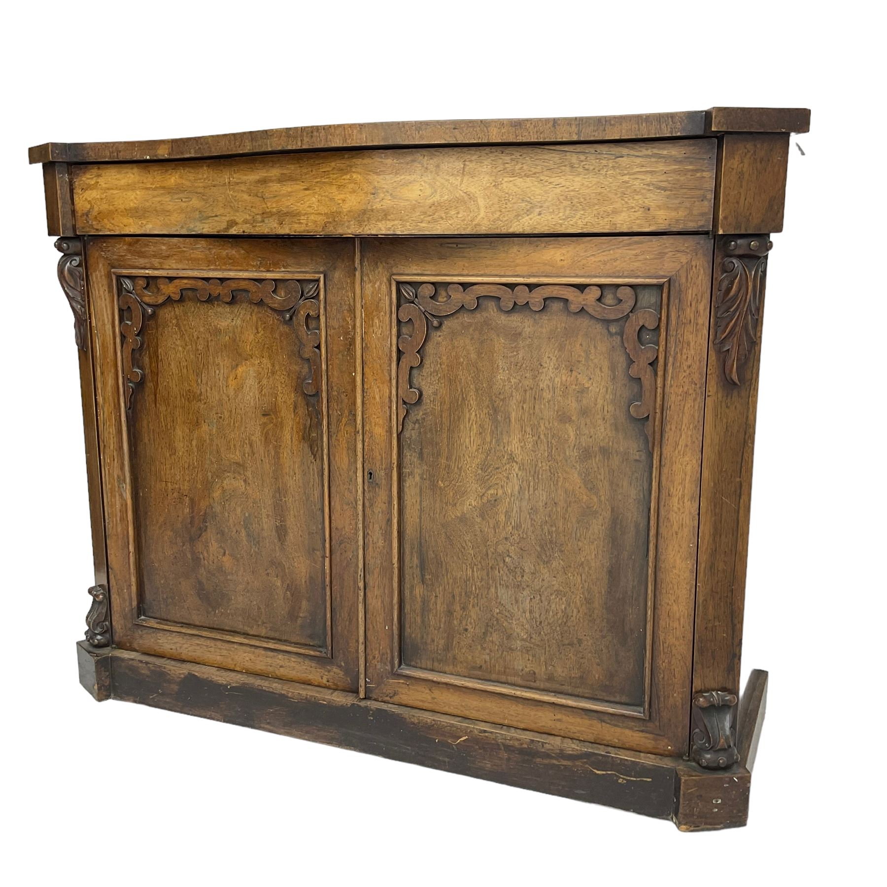 William IV rosewood serpentine chiffonier, fitted with frieze drawer over two panelled cupboard doors with applied C-scroll decoration, flanked by canted uprights with moulded foliate corbels
