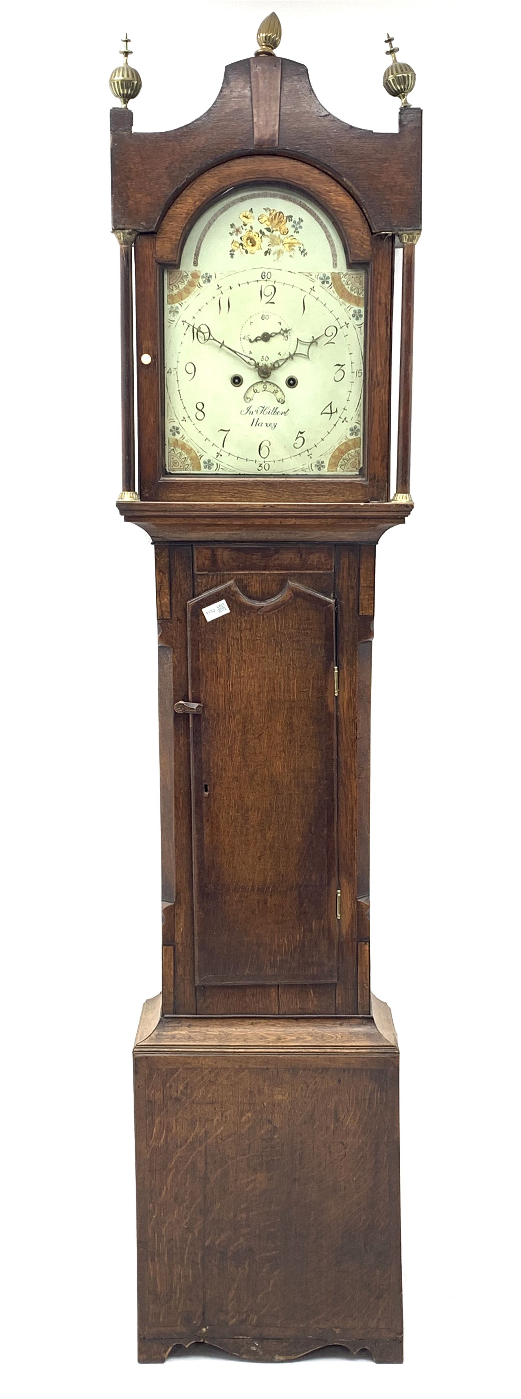 Early 19th century oak longcase clock, shaped pediment over a stepped arch glazed door enclosed by plain pilasters, the case with canted corners and trunk door with sloped arch top and centre curved return, enamel Arabic dial painted with flowers and patterned spandrels, signed 'Jno. Hilbert, Haxby', eight-day movement with subsidiary seconds dial and false calendar dial 