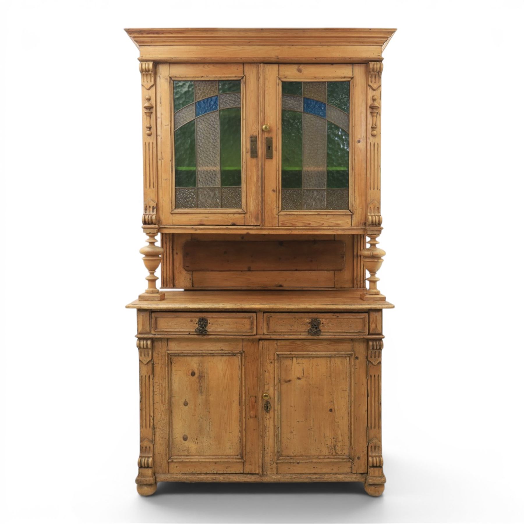 Late 19th century French pine dresser with stained glass upper section, the upper section with projecting cornice with fluted and scrolled details, enclosing a shelved interior, supported on turned front uprights, the lower section with frieze drawers and cupboard doors, raised on bun feet