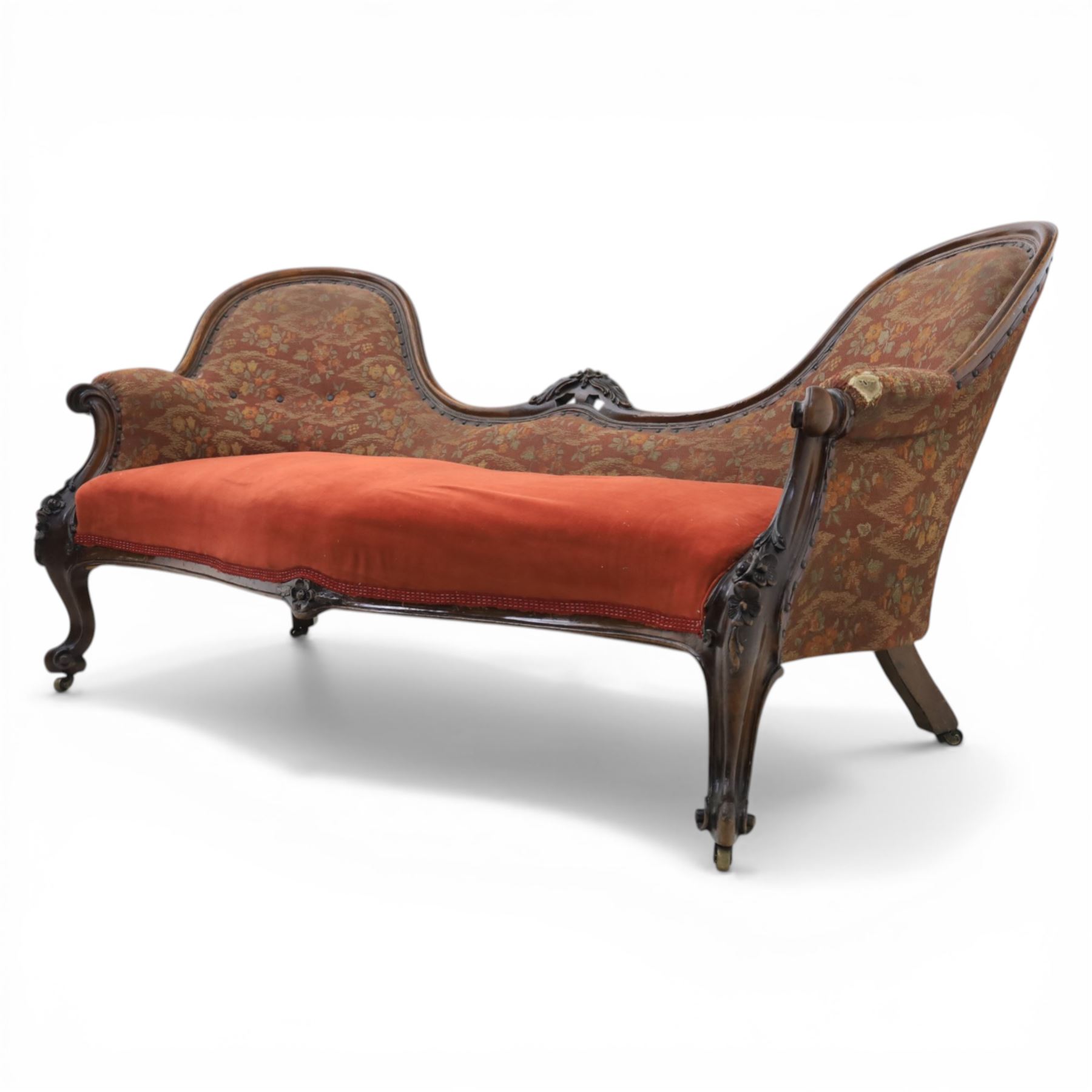 Victorian mahogany framed serpentine sofa, the shaped button upholstered back with central carved foliate cartouche, and scroll arms with carved terminals, over upholstered red seat, upon carved cabriole supports with castors