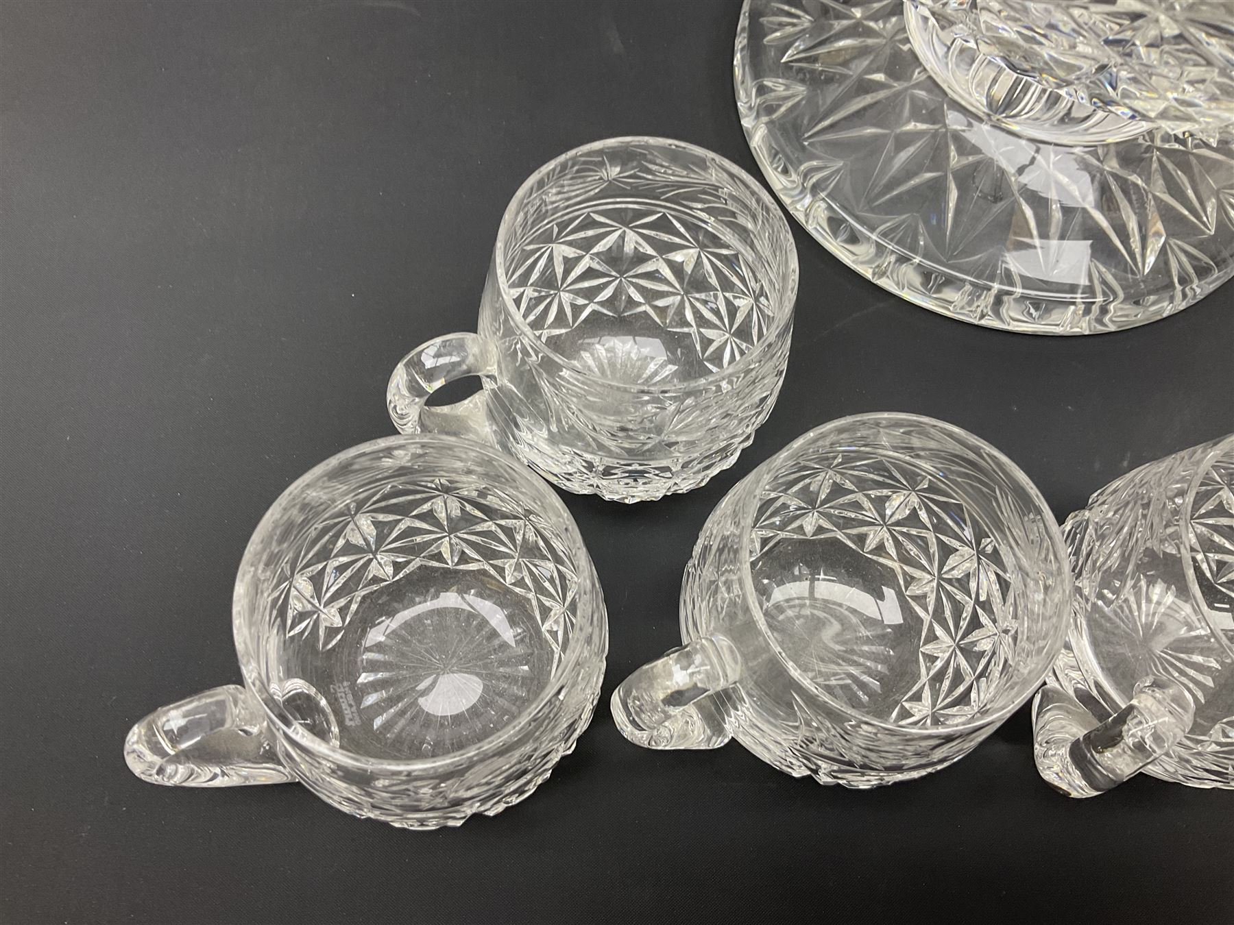 Large Stuart crystal pedestal punch bowl, of circular form, the rim with engraved floral decoration, upon spreading circular foot with radial cut decoration, with seven matching Stuart crystal drinking glasses, each with a C handle, each acid signed beneath, bowl H20cm