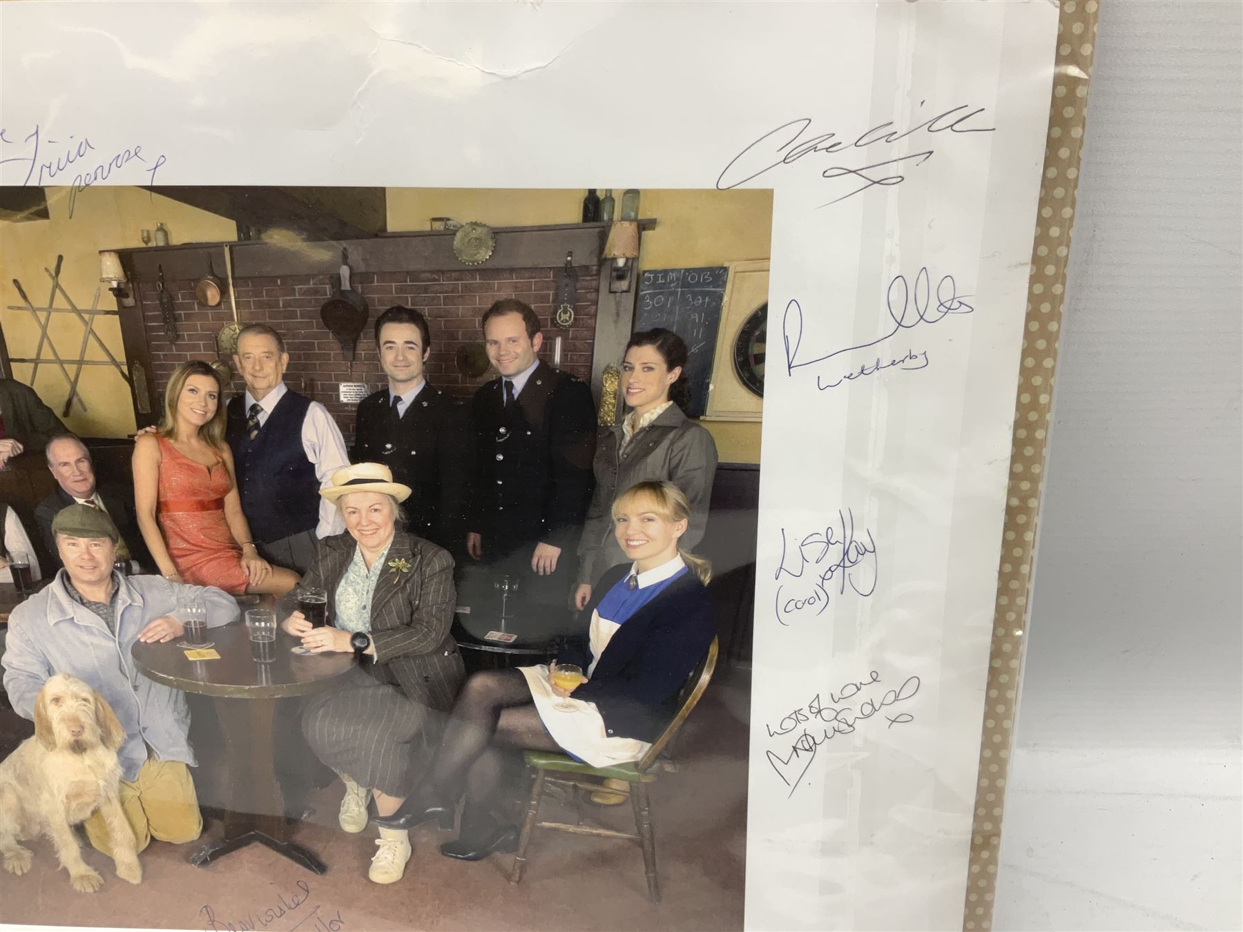 Photograph of the cast of Heartbeat posing in costume in the Aidensfield Arms and signed by twelve cast members including John Duttine, Tricia Penrose, Clare Wille, Derek Fowlds, Gwen Taylor, Lisa Kay, Peter Benson etc; unframed