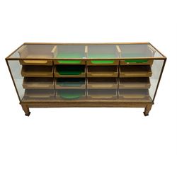 Early 20th century oak framed haberdashery shop counter, glass panel exterior enclosing sixteen graduating drawers with oak fronts and handles, raised on shaped tapering supports 