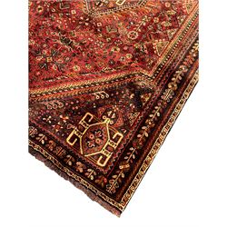 Persian Qashqai red ground rug, the main field decorated profusely with small stylised motifs, central lozenge medallion, multi-band border decorated with trailing foliate and flower head motifs 