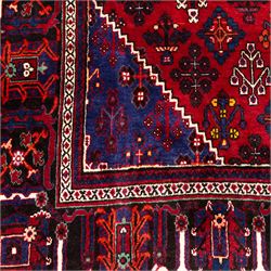 Central Persian Joshagan hand-knotted rug, madder-red field with central stepped lozenge medallion enclosed by angular spandrels, field decorated with repeating stylized geometric floral motifs and small diamond devices enclosed by a dark border of geometric ornament between multiple guard stripes, with cotton fringe ends  