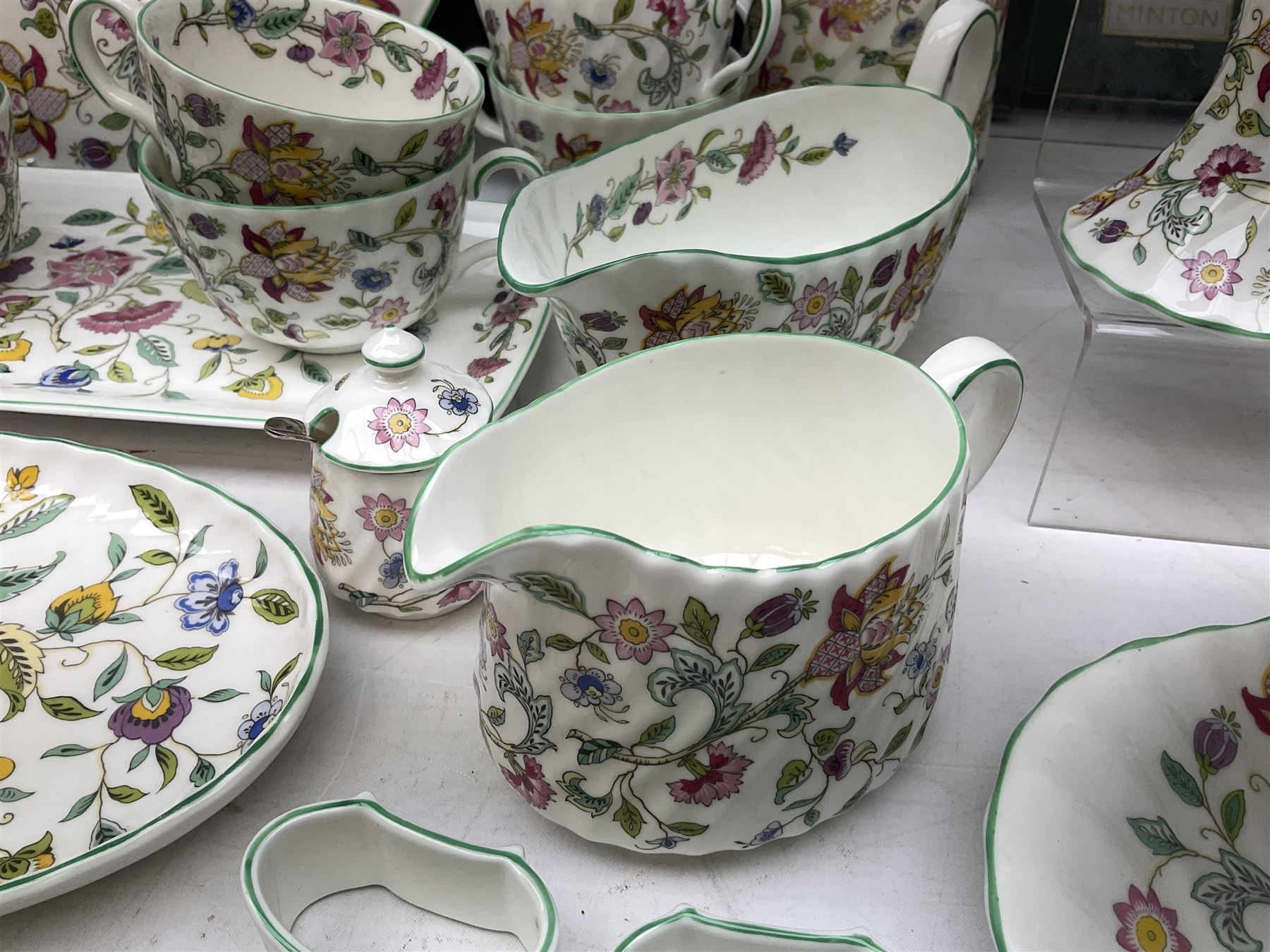 Minton Haddon Hall pattern tea and dinner wares, including basket dish, two covered tureens, six dinner plates, eight dessert plates, twelve tea plates, six soup bowls, six cereal bowls, teapot, coffee pot, milk jug, covered sucrier twelve tea cups and saucers, six mugs, footed bon bon dish, pair of candlestick holders, cake knife and slice etc (81)