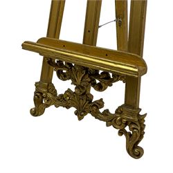 Victorian design gilt floor standing picture easel, the C-scroll and leaf decorated pediment over the moulded frame with upper extending flower head decoration, the apron and terminals in the form of S-scrolled foliate and central fanned leaf cartouche, with adjustable picture rest  