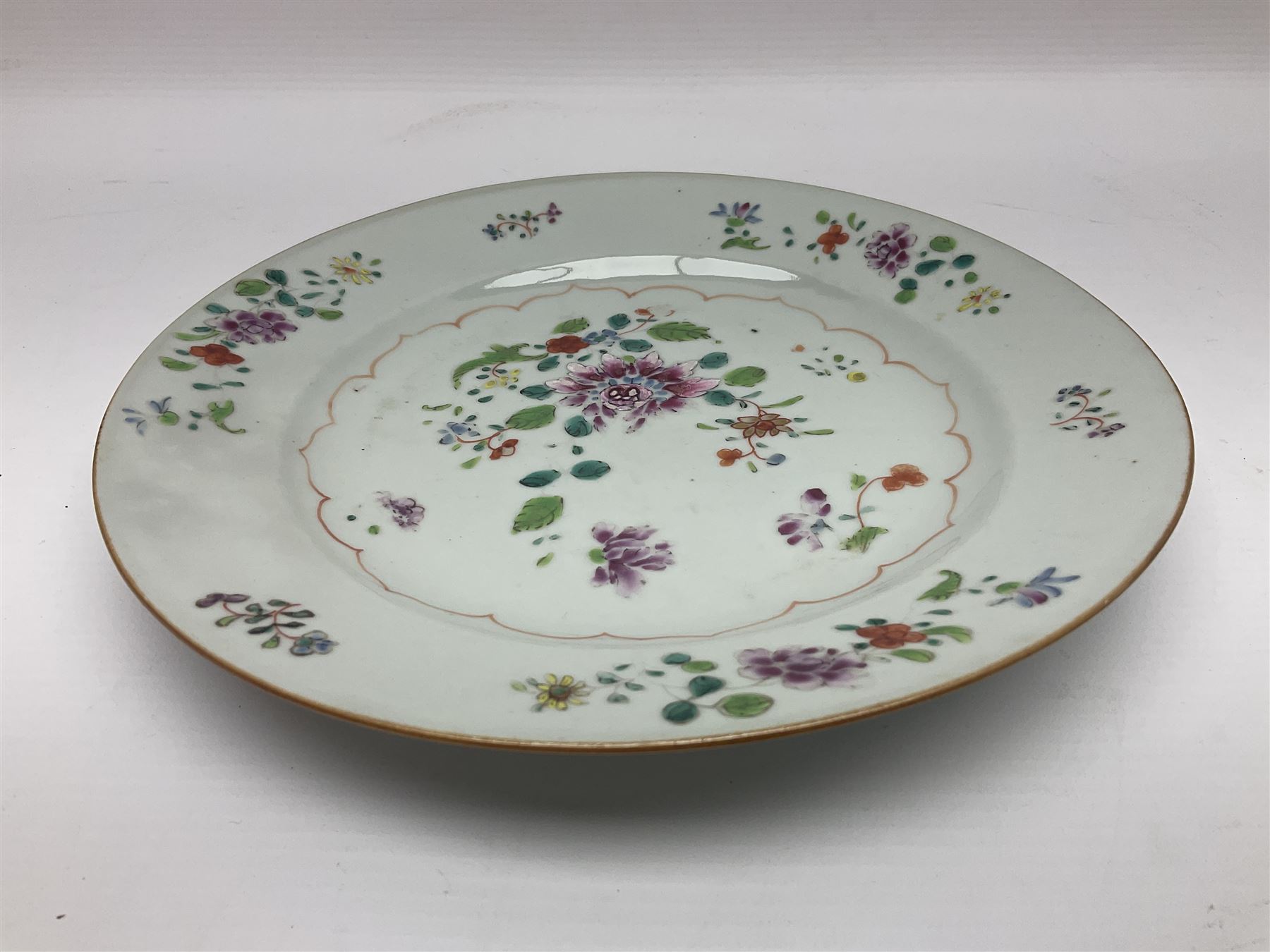 Three 18th century Chinese Famille Rose plates, the first example enamelled with blossoming peonies, rockwork and fence, the other two examples of similar design, decorated with blossoming peonies and sprigs within shaped inner borders, each approximately D23cm