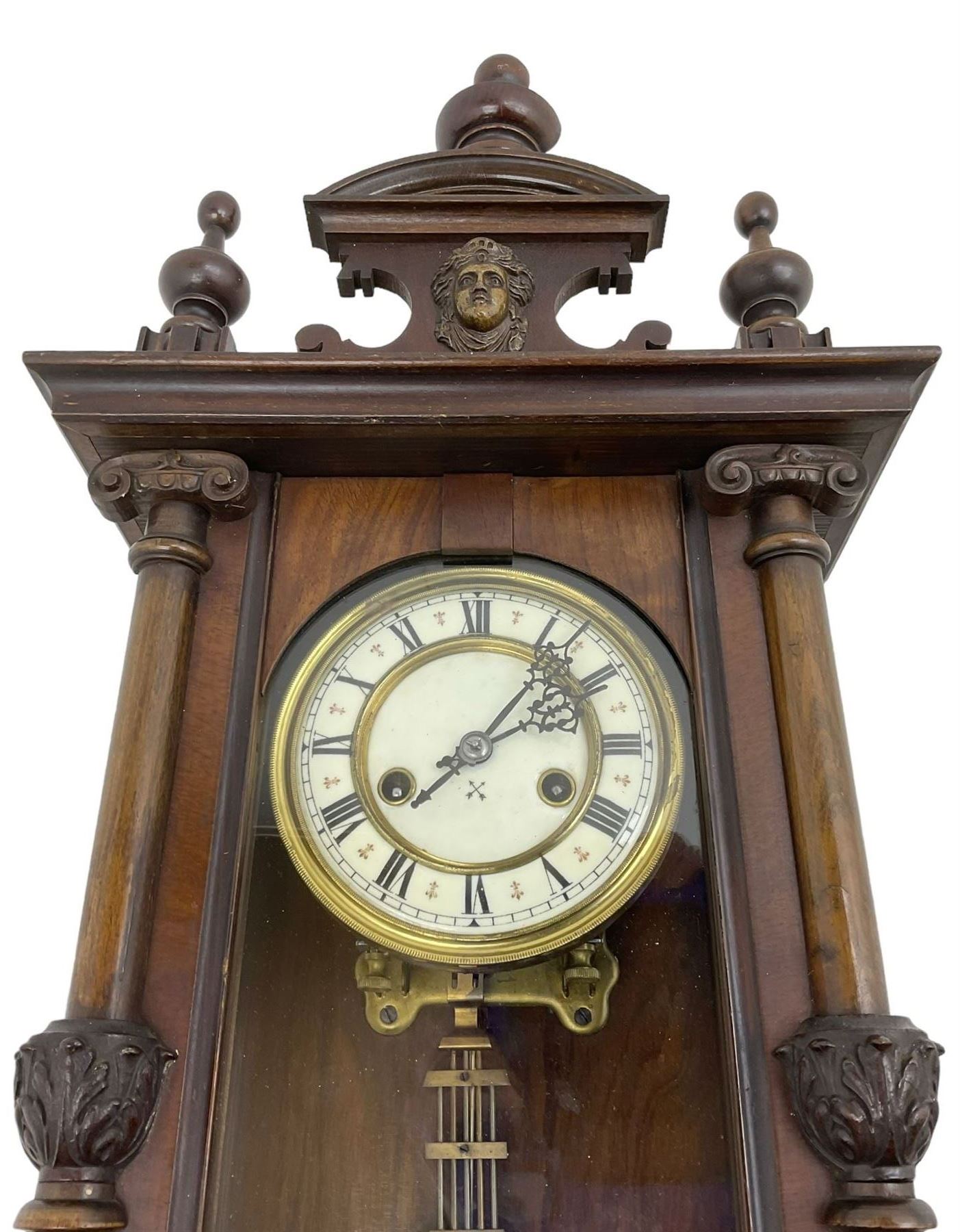German - Hamburg American Clock Company Vienna style 8 day wall clock c 1900, mahogany case  with a carved pediment and finials, fully glazed case door with attached pilasters and carved ionic capitals, two part dial with Roman numerals and pierced steel hands, with a gridiron pendulum and twin train spring driven countwheel striking movement.
