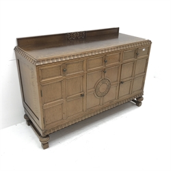 E. Gomme Ltd of High Wycombe oak sideboard, raised carved back, moulded top, three drawers above two cupboards flanking single fall front unit, turned supports joined by stretchers, W150cm, H101cm, D57cm