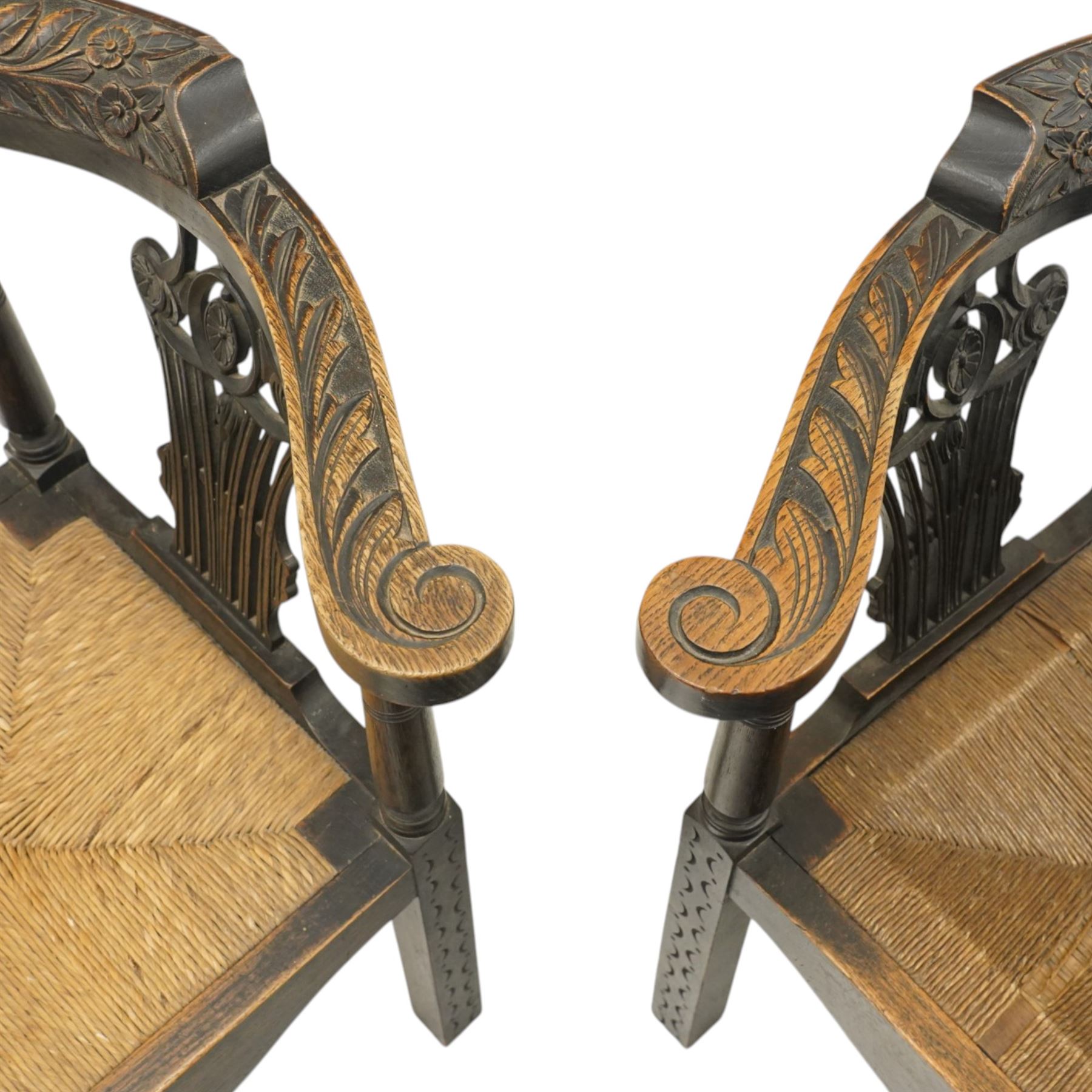 Pair of 19th century carved oak corner chairs, cresting rail carved with central floral bouquet with trailing foliage extending to the scroll arm terminals, pierced back splats with rosette motifs over drop-in rush seats, front cabriole support with acanthus carved knee and ball-and-claw foot