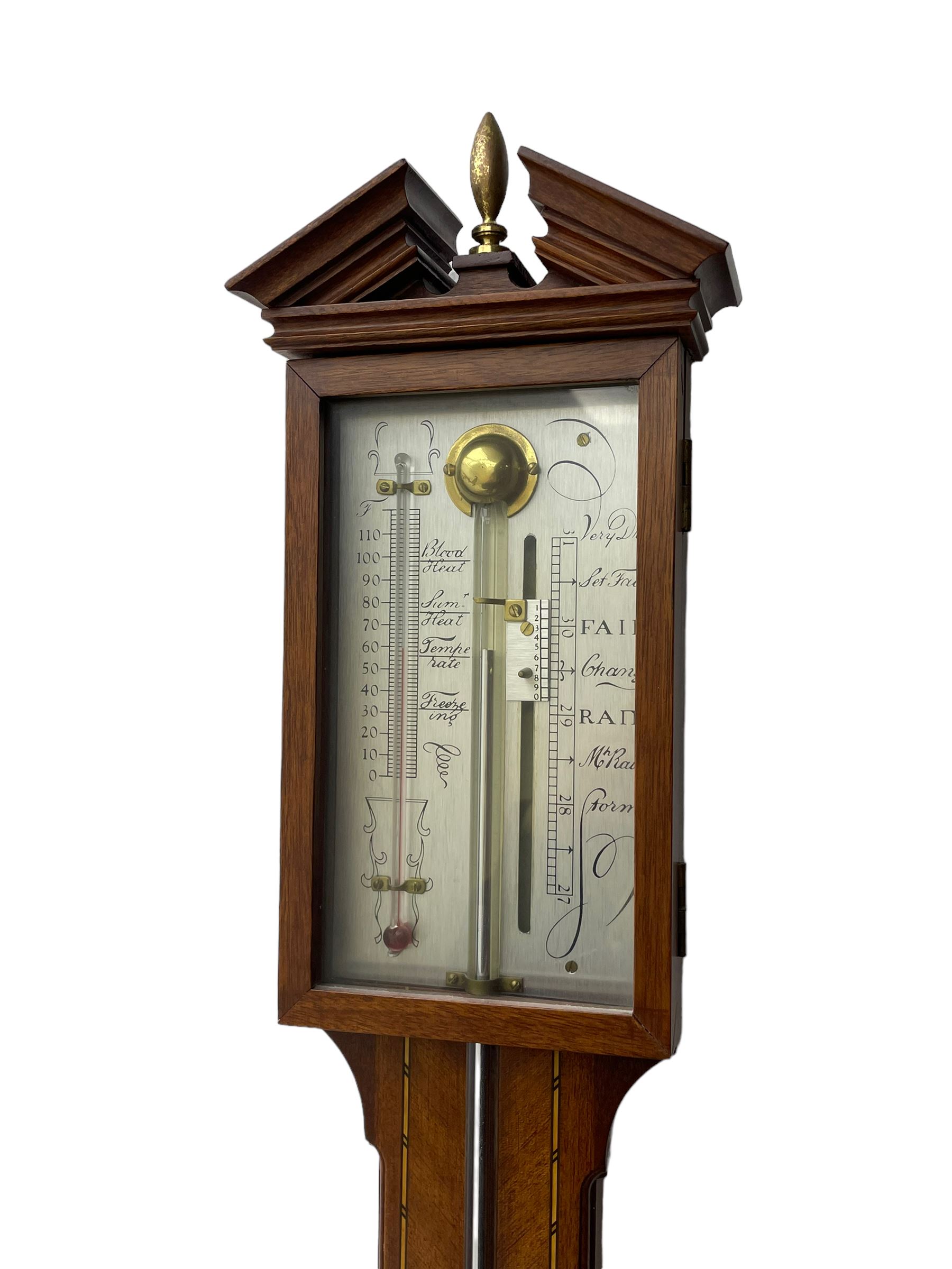 20th century - mercury cistern barometer in an 18th century style mahogany case with contrasting inlay and a broken pediment, round base with a turned cistern cover, fully exposed glass tube and silvered register within a glazed door, with a Fahrenheit spirit thermometer, engraved weather predictions and sliding vernier. Mercury clean and present.
