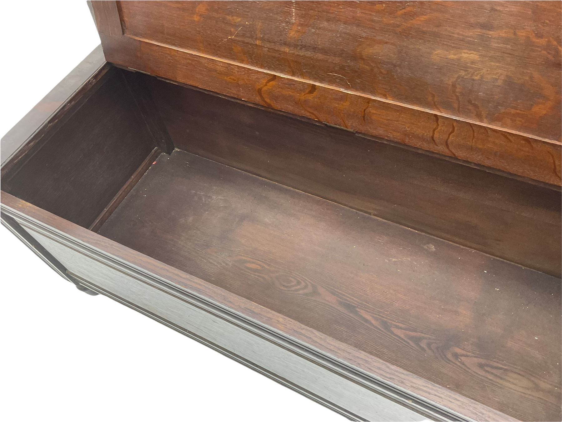 Late 19th century oak settle bench, shaped cresting rail carved with ribbon over triple panelled back, the panels relief carved with scrolled and floral urns and cartouche, hinged box seat, turned front feet, with upholstered squab cushion