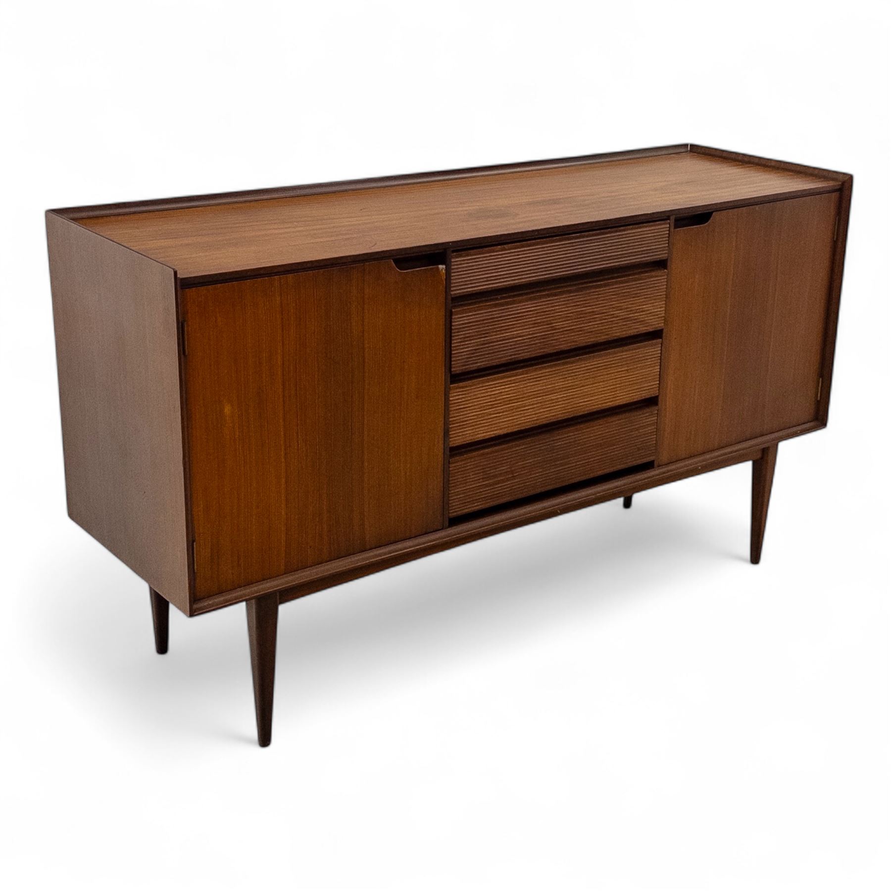 Richard Hornby for Fyne Ladye - mid-20th century afromosia teak sideboard, retailed by Heals of London, rectangular form, with low profile carved gallery lip, above three central drawers with ribbed drawer fronts, flanked by two cupboards with vertically grained doors and recessed pull handles, with streamlined moulded edges and sides, raised on tapered slender legs 