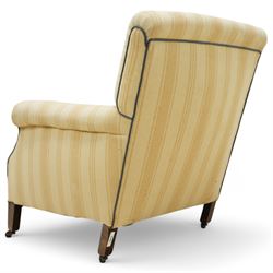 Early 20th century scroll arm armchair, upholstered in ivory striped cotton fabric with piped seams, sprung seat, on turned tapering front legs with brass caps and castors