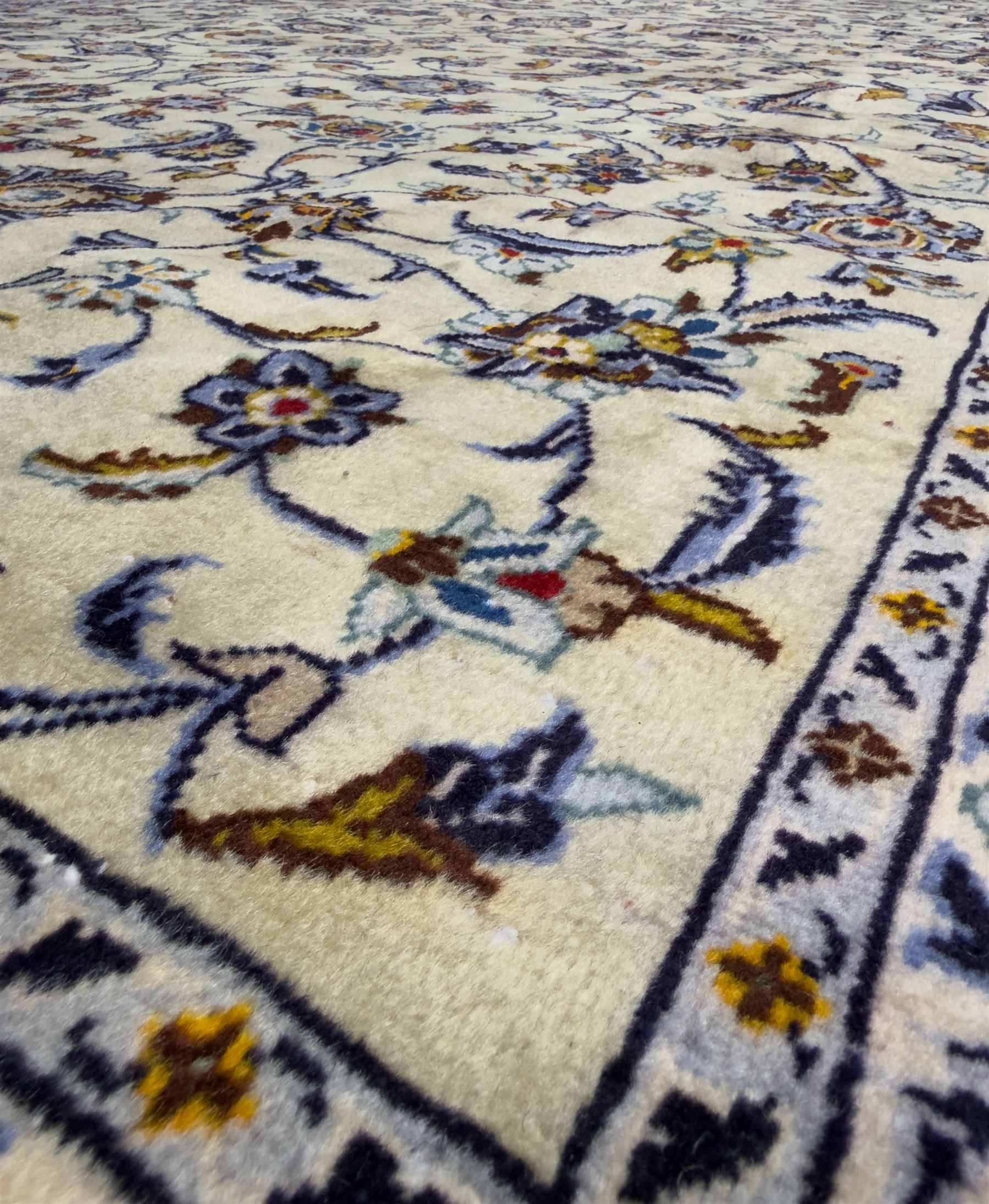 Central Persian Kashan hand-knotted carpet, ivory field with an all-over design of scrolling vines, lotus palmettes, and rosettes in shades of blue, gold, and brown within a blue ground border of palmettes and arabesques between multiple guard stripes