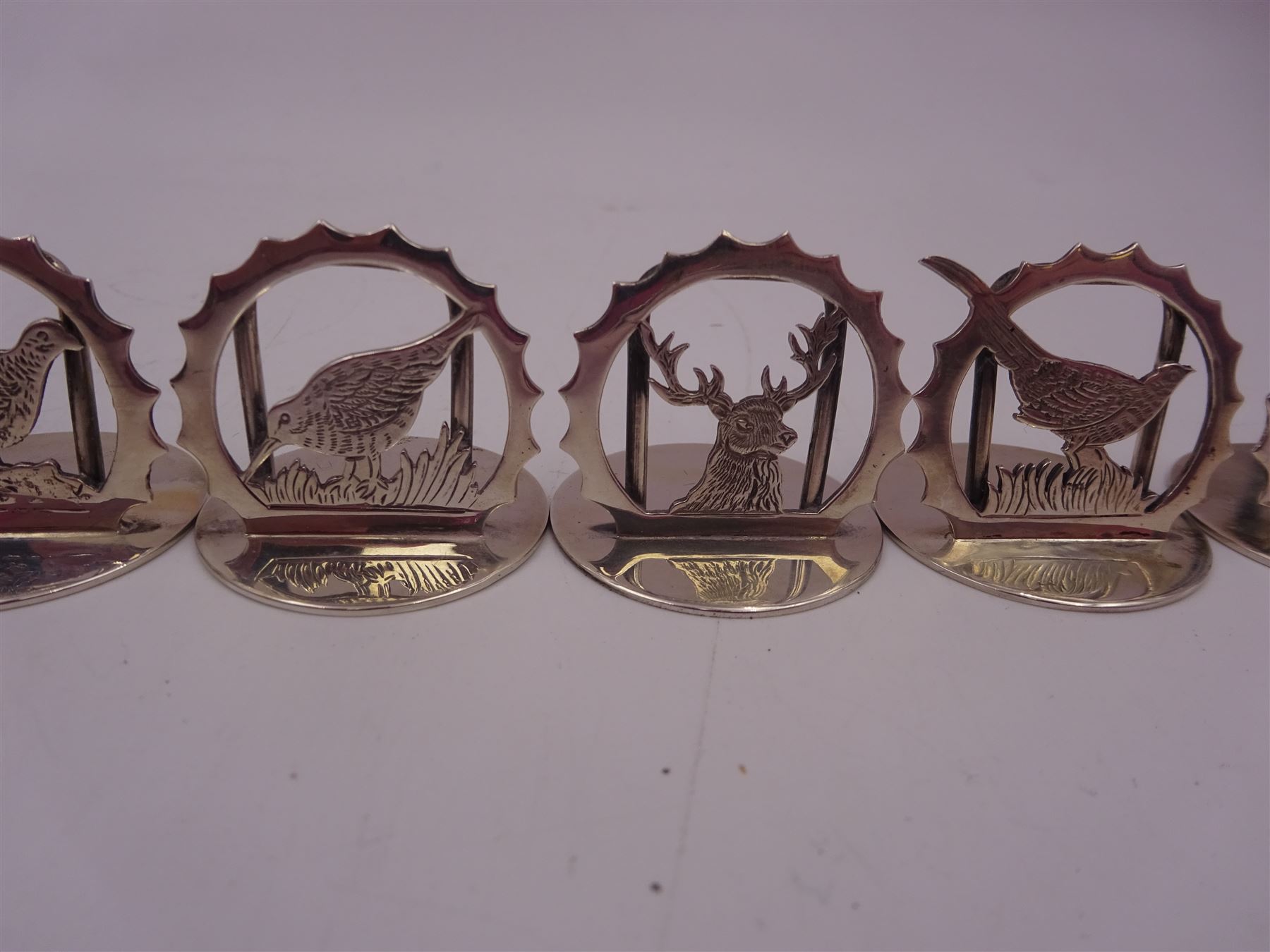 Set of six modern silver place card holders, each of circular form with pierced depictions of a partridge, spaniel, pheasant, stag, woodcock and duck, hallmarked J A Campbell, London 1985, contained within a velvet and silk lined fitted case, H3cm
