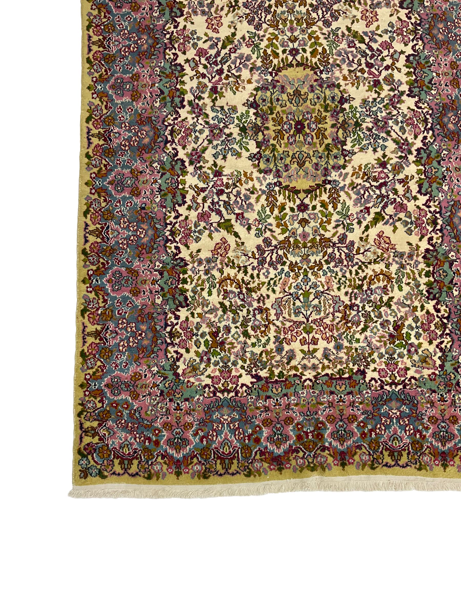 Central Persian Kirman ivory ground rug, decorated all-over with flower heads and trailing foliage, shaped pink and blue ground borders with olive green outer band