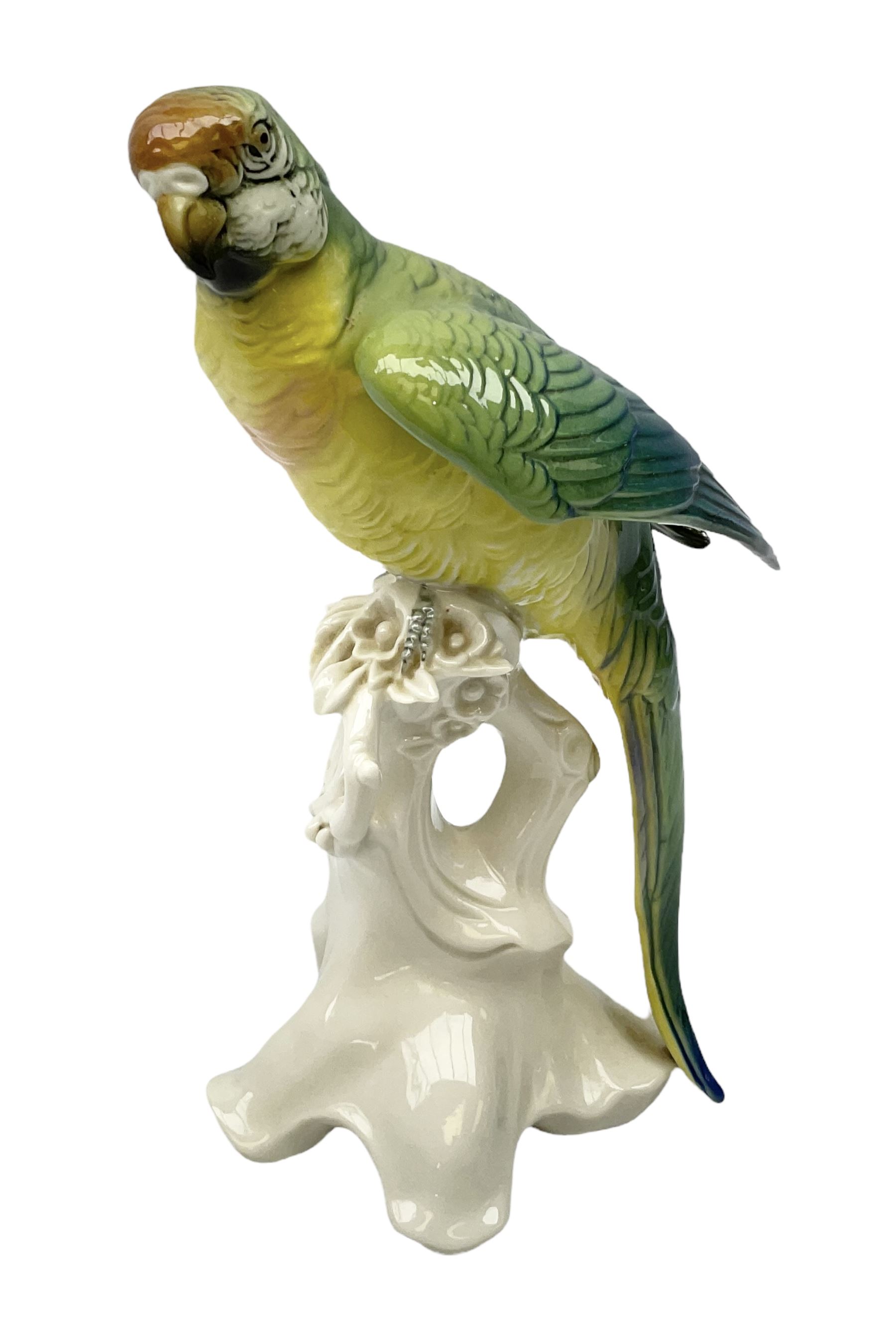 Karl Ens porcelain figure of a parrot, modelled with yellow breast, blue back and wings and green tail, perched upon on a blossoming branch, with blue printed factory mark beneath, H24.5cm