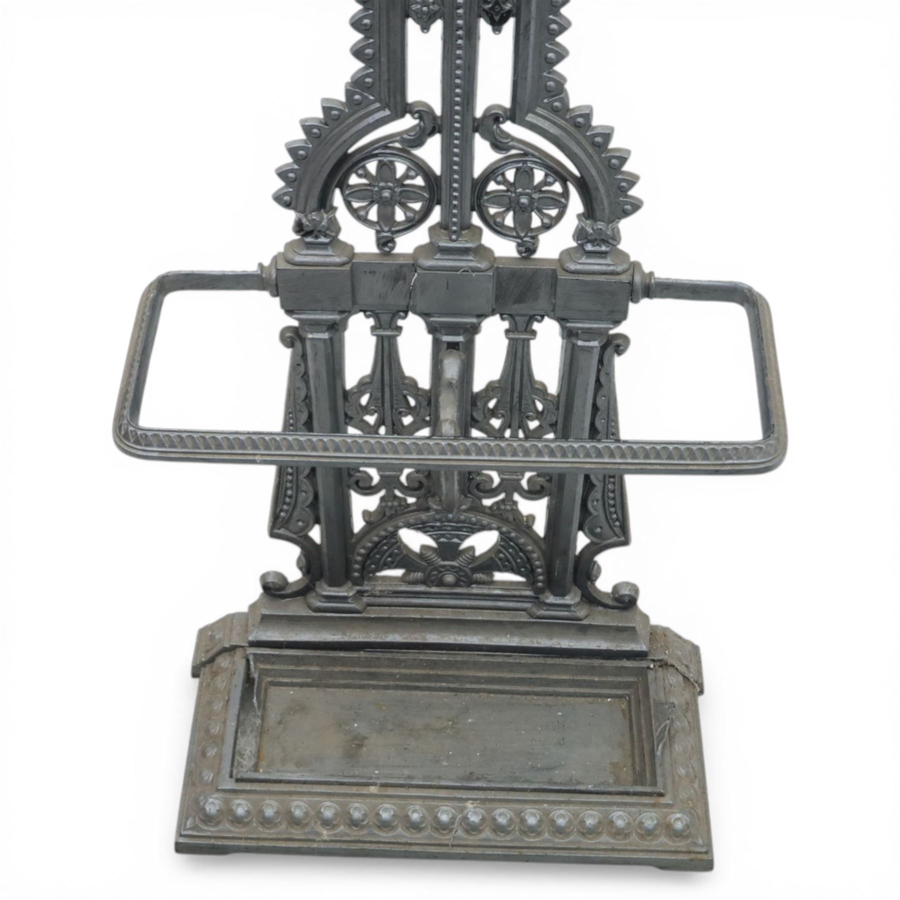 Late 19th century cast iron hall stand in the style of Christopher Dresser, cross shaped upper section with radiating wheel motif and applied hooks, architectural upright with pierced Gothic and geometric detail, fitted with rectangular drip tray and pierced surround, raised on stepped plinth base with bead decoration