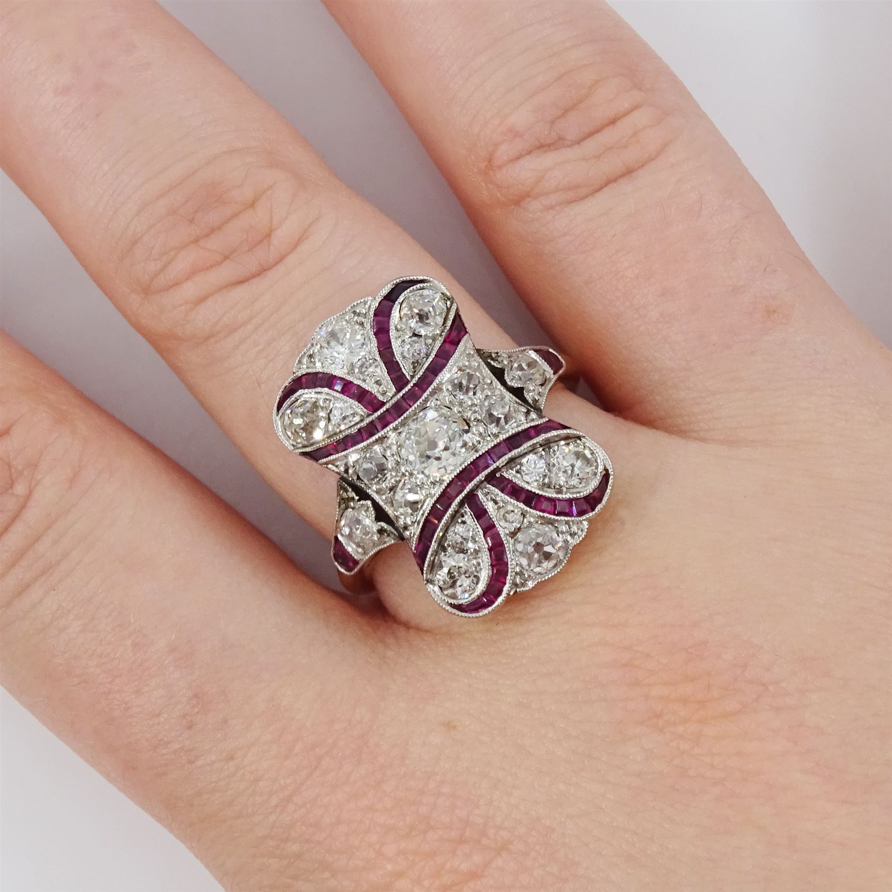 Early 20th century gold and platinum ruby and diamond panel ring, the principal old cut diamond of approx 0.30 carat, with old cut diamond surround and milgrain set calibre cut ruby ribbon motif, the tulip head shoulders set with a further diamond and ruby, total diamond weight approx 1.75 carat