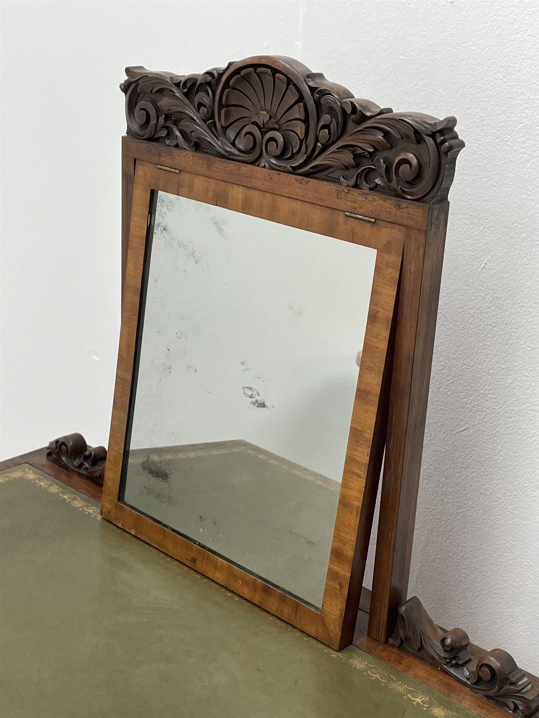 Early Victorian figured mahogany dressing cabinet, the raised shell and scroll carved back lifts to reveal rectangular easel mirror with mahogany band, flat rectangular top with tooled leather inset, slide at each side with matching leather inset, full width drawer above cupboard enclosing a series of five drawers, turned front supports, panelled front, sides and back