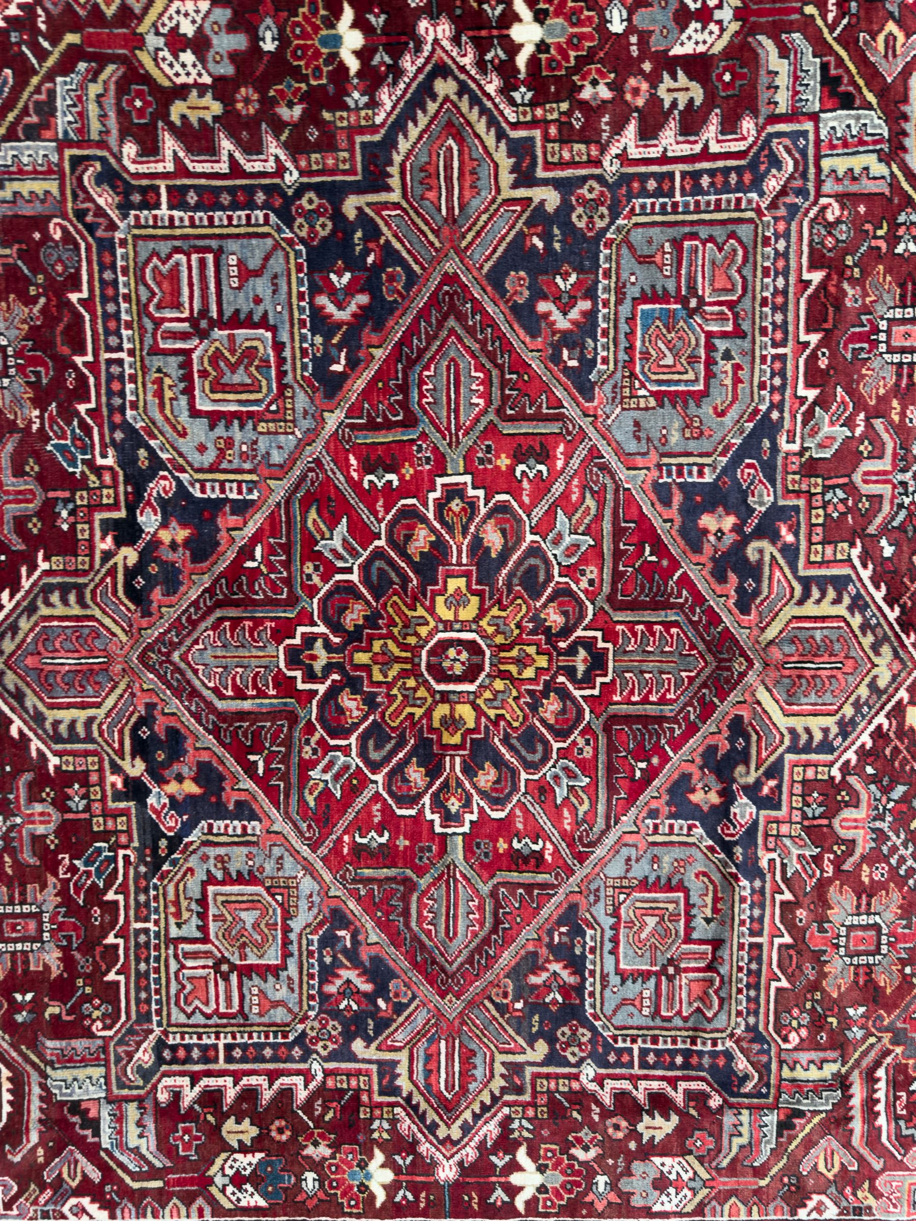 Northwestern Persian Heriz carpet, the madder red field centred by a large octofoil medallion with serrated edge, flanked by ivory stepped spandrels and geometric floral motifs in indigo, ochre and sky blue, enclosed by a navy border of rosettes and angular vines, from the region of Heriz