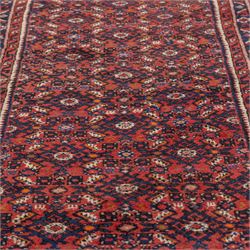 North West Persian Malayer hand-knotted runner, decorated with a dense all-over pattern of small repeating boteh and rosette motifs on a rich madder red ground, field filled with geometric floral elements arranged in a lattice design, framed by a narrow main border and flanked by slender guard borders, with cotton fringe ends 