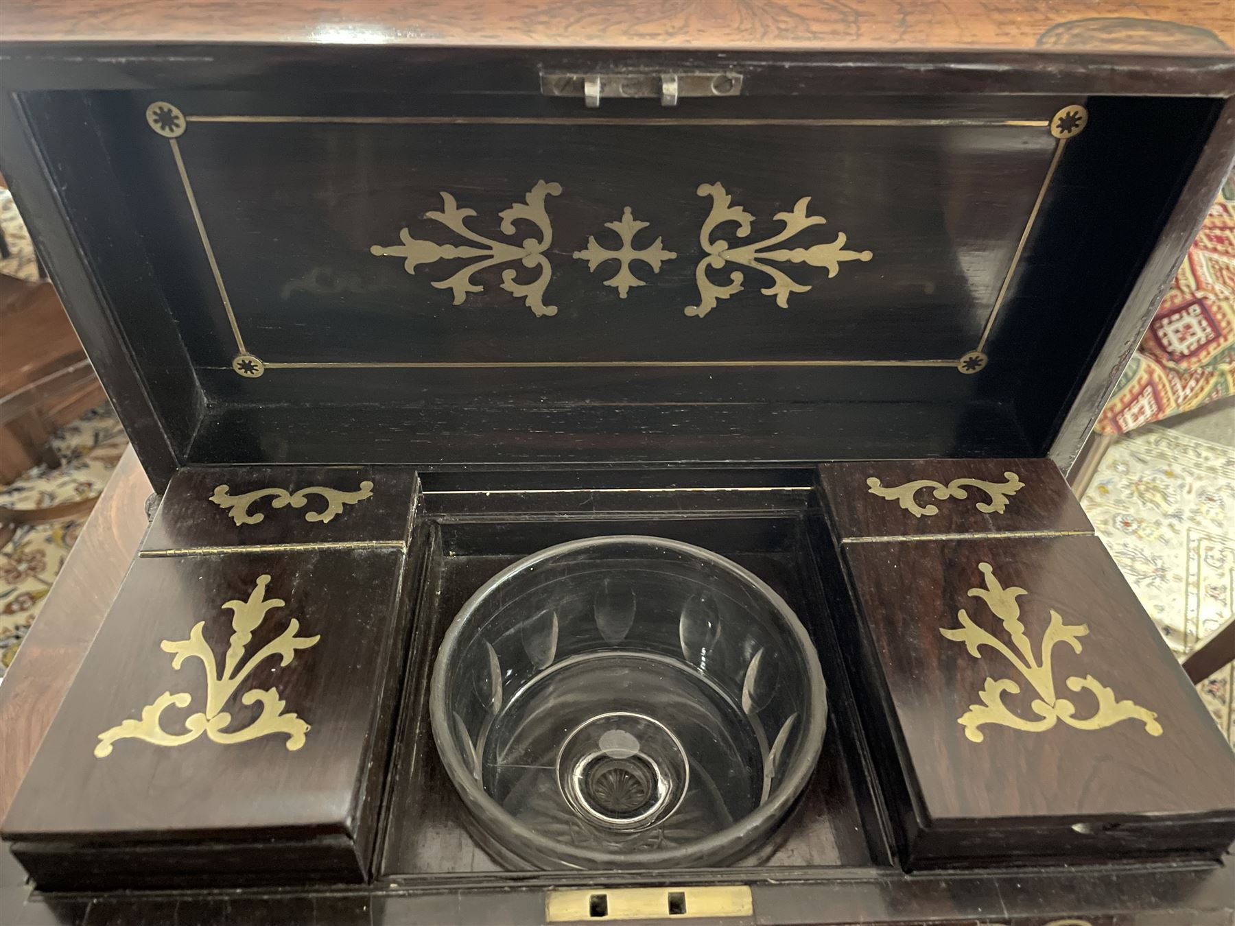 Early 19th century rosewood and brass inlaid tea caddy, of sarcophagus form, the front and hinged opening cover inlaid with brass scrolling panels, opening to reveal a compartmented interior with twin removable boxes with conforming inlaid brass detail to the hinged covers and zinc lining to the interiors, flanking a later glass mixing bowl, the whole upon four turned cylindrical feet, H21cm W36cm D20cm