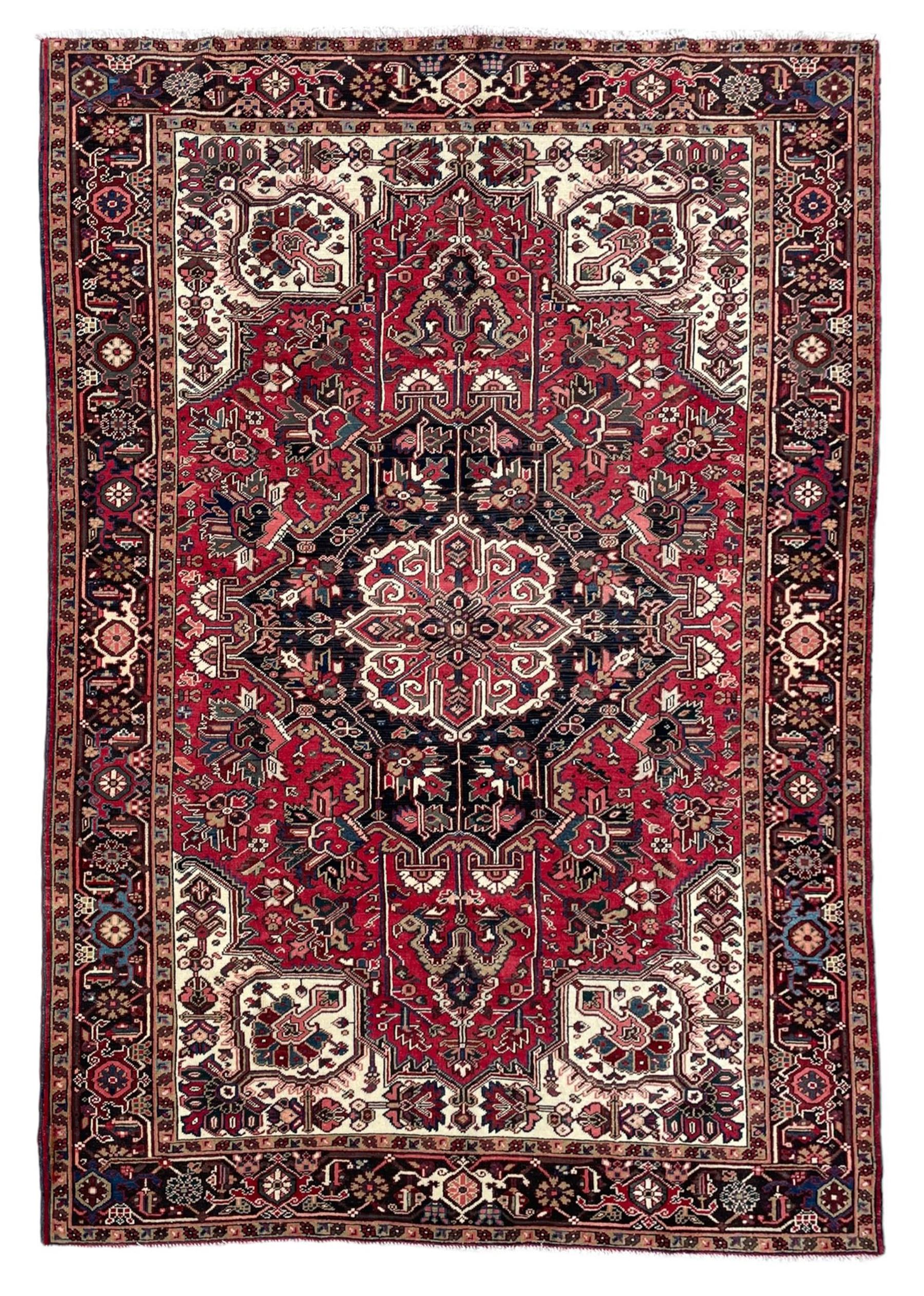 Persian Heriz red ground rug, central scrolled medallion on dark ground decorated with floral motifs, the surrounding field decorated with stylised plant motifs and smaller geometric symbols, guarded border with repeating pattern punctuated with rosettes and flower heads 