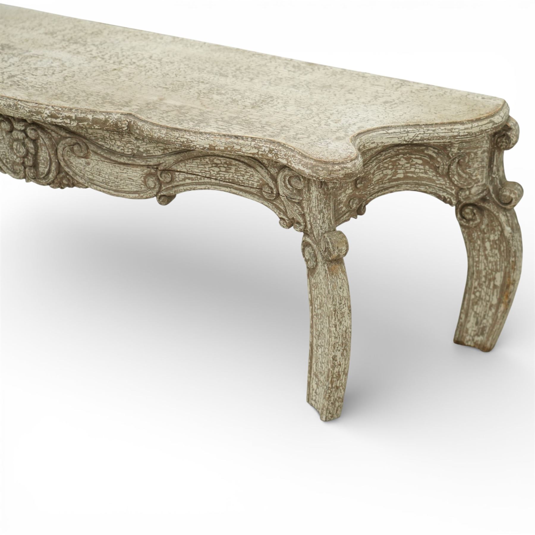French style low console table, the shaped rectangular top with undulating outline and moulded edge, worn painted finish throughout, the frieze carved with flowing C-scrolls, shell and foliate detail centred by a floral reserve, on cabriole legs with carved knees and inward curving feet