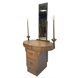 Art deco oak dressing table, raised back with rectangular swing mirror, oval top with flanking electric candlesticks, the frieze with central floral panel and two drawers, over two central drawers