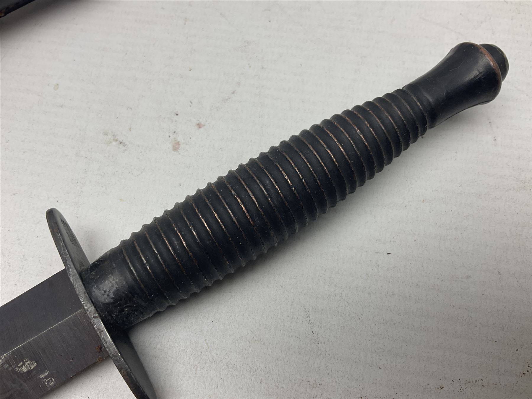 Third Pattern Commando Knife or Dagger with 17.5cm flattened diamond section blade and regulation black painted ribbed copper hilt with brass pommel nut; stamped William Rodgers Sheffield England to the cross-piece; in black painted brass mounted leather scabbard L34.5cm overall