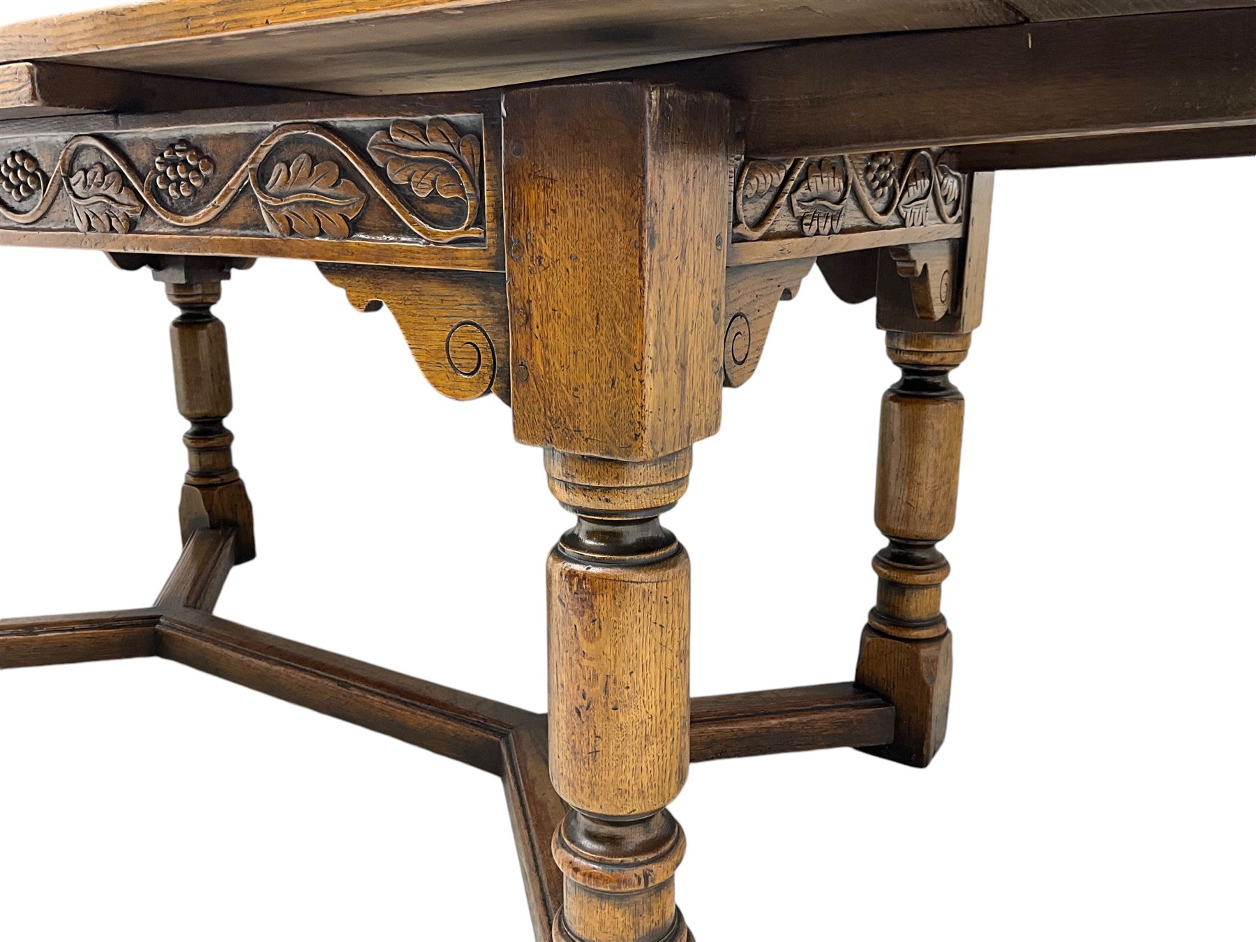 Early 20th century Jacobean design draw-leaf oak dining table, rectangular top with carved frieze depicting scrolling foliage and grape clusters, sliding extending leaves, raised on robust turned supports united by H-stretcher  