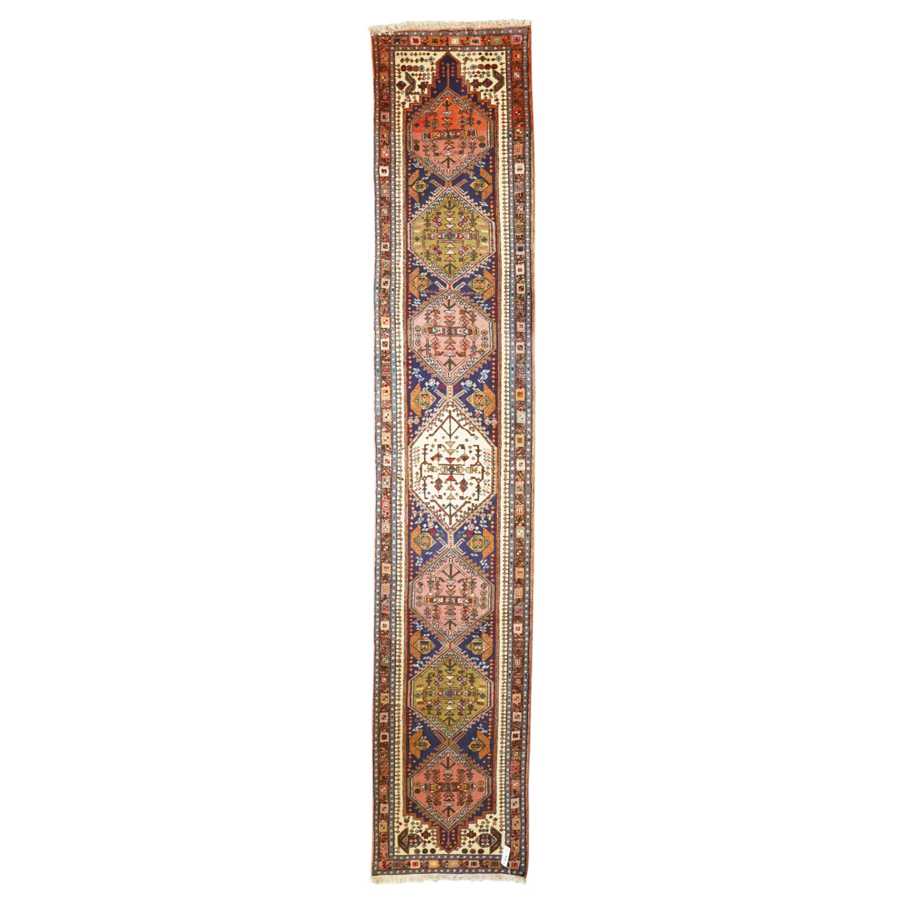 Persian Iranian wool runner, with a series of stepped hexagonal medallions in rust, olive and ivory against and deep navy field, the medallions are filed with floral and latch-hook motifs, framed by and ivory guard border with geometric rosettes, flanked by a rust outer band