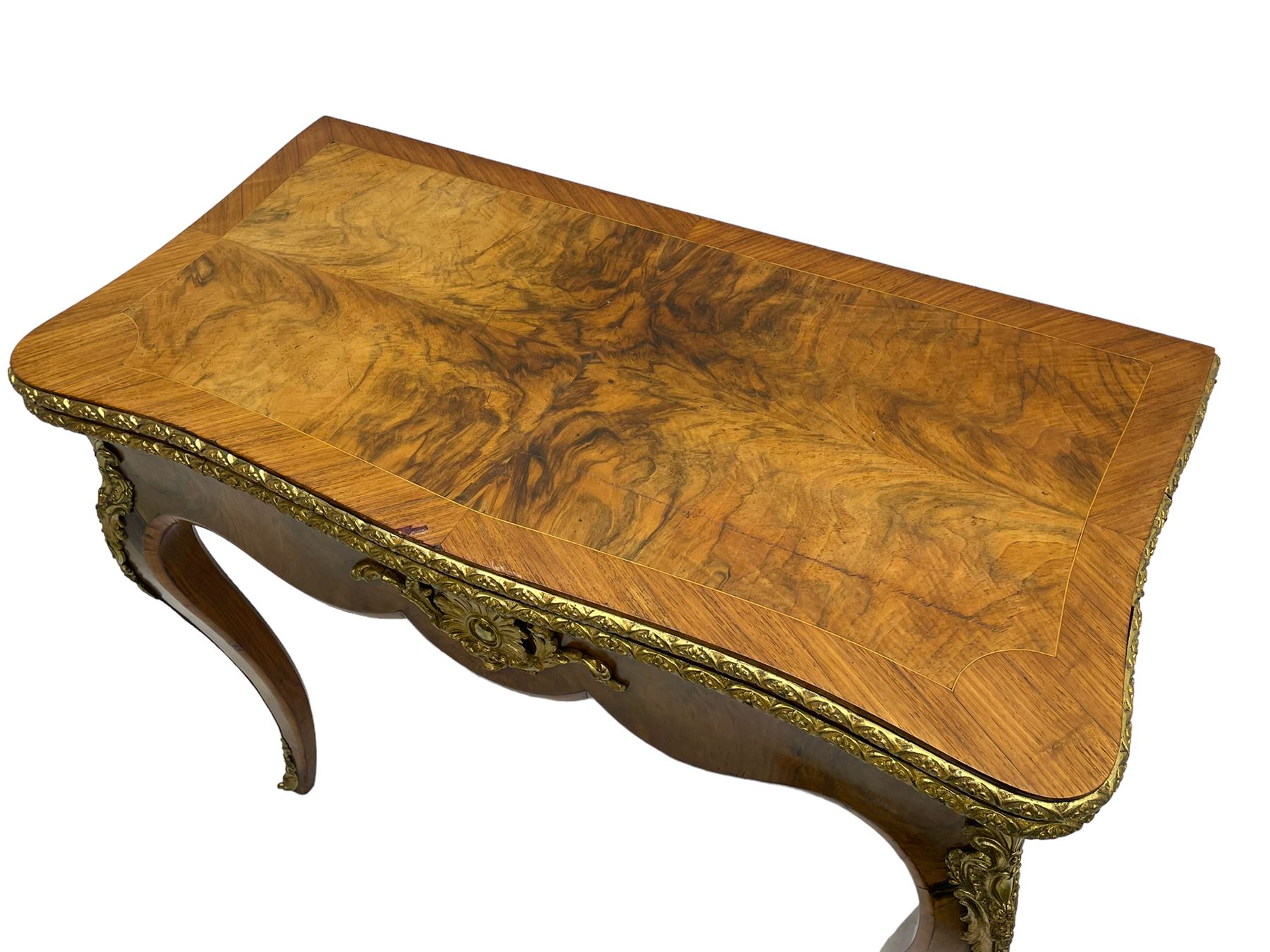 20th century French walnut and Kingwood card table, shaped fold-over top with figured quarter-matched veneers and floral egg and dart moulded edge in gilt metal, shaped aprons decorated with shell motifs with extending foliage, pull-out action base revealing storage well, on cabriole supports with ornate gilt metal mounts 