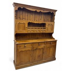 Traditional vintage pine kitchen dresser with scrolled cornice and rack with long shelf above a galleried shelf flanked by three short drawers and two cupboards, the base with three long drawers above three cupboards on plinth base  