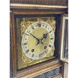 Late Victorian oak mantel clock in architectural case, sloped pediment flanked by two raised turned finials, reeded frieze and returns, brass dial with Roman silvered chapter ring, ornate cast winged putti spandrel, twin train quarter chiming ‘Ting Tang’ movement striking on coils